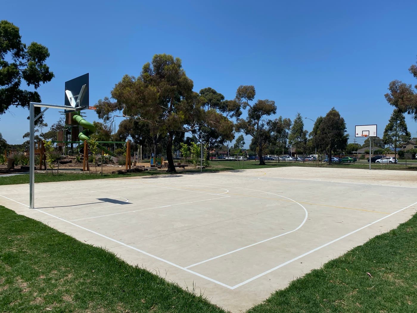 Finished concrete basketball court with line marking, playground behind